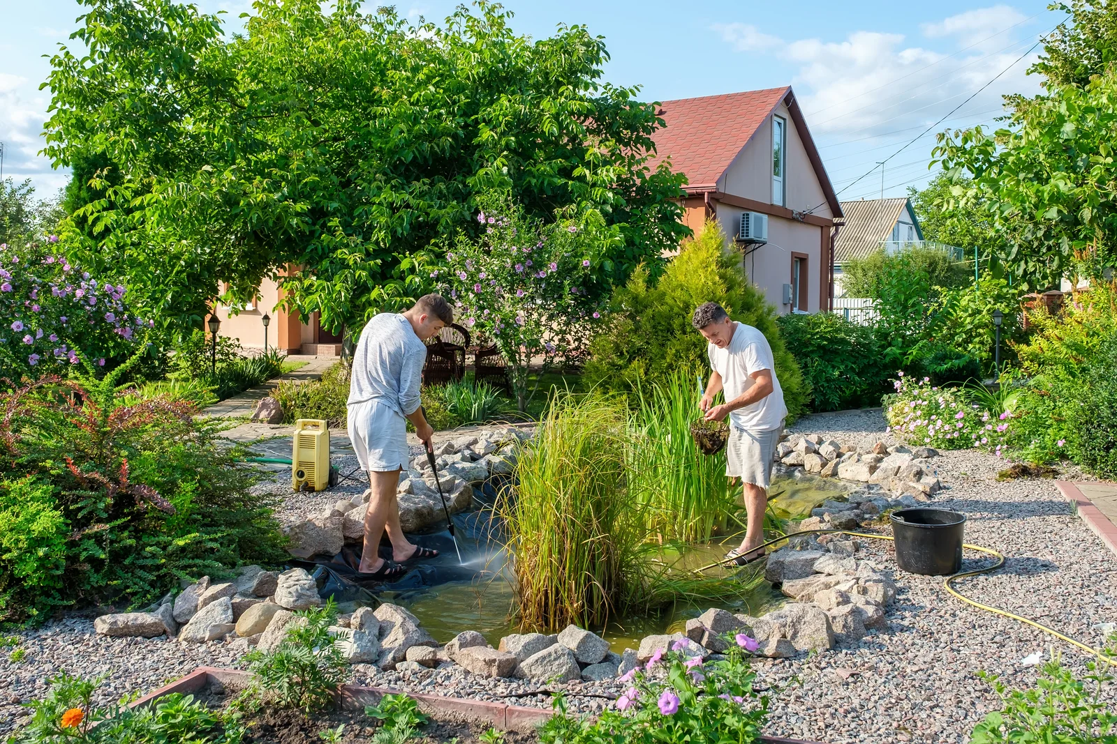 Zwei Teichreiniger beim Entfernen von Algen und Teichschlamm in einem privaten Gartenteich in Wandlitz